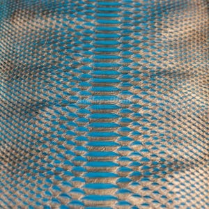 Può includere: Un materiale testurizzato con un motivo ripetitivo di squame sovrapposte in una finitura bronzo metallizzato. Gli spazi tra le singole squame rivelano un colore blu brillante, creando un effetto visivo ad alto contrasto.