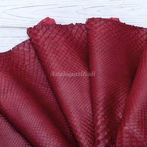 May include: A deep red, textured material with a distinct scale pattern resembling snake skin. The surface features a repeating diamond-shaped scale structure throughout. The text AcalapatiBali is visible in the center of the material.