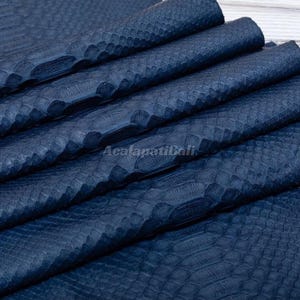 May include: A dark blue sheet of textured material featuring a repeating scale pattern across the surface. The material is folded into multiple layers, creating deep ridges and shadows. The text Acalapatibali is visible in the center.