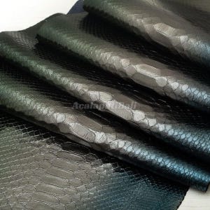 Peut inclure: Plusieurs couches de cuir vert métallique foncé avec un motif texturé en relief façon peau de serpent. Le matériau présente une finition brillante qui reflète la lumière sur les écailles, créant un aspect profond avec un filigrane visible.