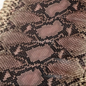 Peut inclure: Un matériau en peau de serpent texturé présentant un motif répétitif de petites écailles superposées dans des tons de rose poudré, de brun sourd et de noir. La surface affiche une grille géométrique distincte de lignes sombres.