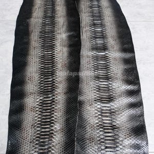 May include: Two long, flat strips of genuine snakeskin leather featuring a gradient pattern. The centre of each strip is a light grey, transitioning into dark charcoal and solid black edges. The scales are textured, overlapping, and uniform.