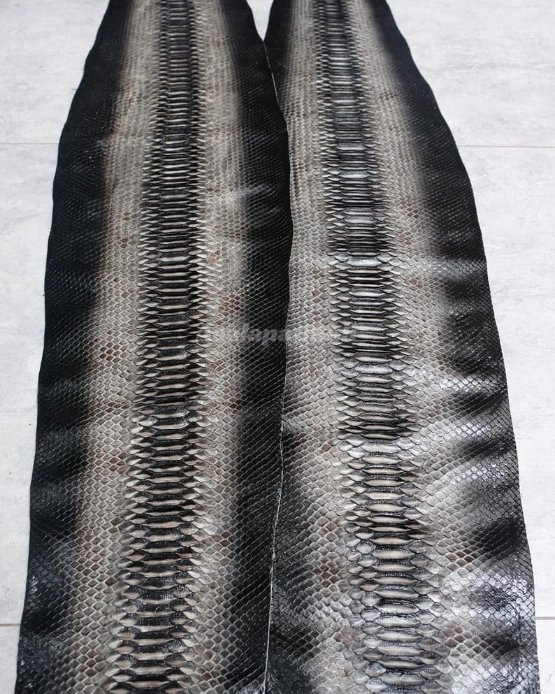 May include: Two long, flat strips of genuine snakeskin leather featuring a gradient pattern. The centre of each strip is a light grey, transitioning into dark charcoal and solid black edges. The scales are textured, overlapping, and uniform.