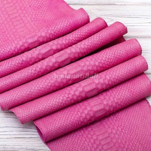 Peut inclure: Une feuille pliée de matériau rose vif présentant un motif d'écailles répétitif et texturé sur toute la surface. Le matériau est disposé en plusieurs plis horizontaux, mettant en valeur la texture gaufrée semblable à de la peau de serpent.