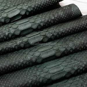May include: A dark forest green snakeskin leather material featuring a distinct, repeating scale pattern with a textured surface. The material is folded in multiple layers, showcasing the natural, organic arrangement of the scales and the deep, matte green coloration throughout the hide.