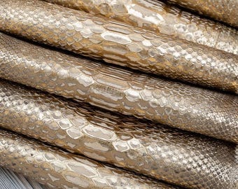 May include: Several rolls of metallic gold material featuring a raised, textured snakeskin pattern. The surface has a reflective, glossy finish with repeating scale shapes arranged in horizontal rows across each cylindrical roll.