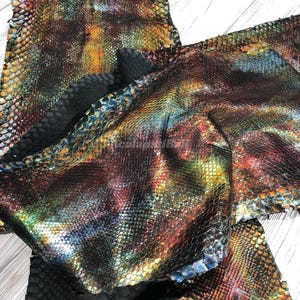 May include: Multiple pieces of iridescent snakeskin leather featuring a multi-coloured scale pattern in shades of blue, green, yellow, and red. The material has a textured, reptilian surface with a metallic sheen and a black underside.