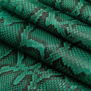 Peut inclure: Une feuille de matériau texturé présentant un motif répétitif de peau de serpent vert émeraude et noir. La surface affiche un design détaillé d'écailles superposées avec des contours noirs profonds et des centres vert vif, créant un effet réaliste.