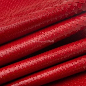 May include: A vibrant red snakeskin leather material featuring a distinct, repeating scale pattern across the surface. The texture is glossy and folded into multiple layers, with the text AcalapatiBali visible in the center of the image.