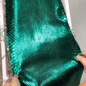 Peut inclure: Une pièce rectangulaire de matériau vert émeraude présentant une texture répétitive et en relief semblable à des écailles sur toute sa surface. Le matériau affiche un éclat métallique et réfléchissant qui capte la lumière, créant des nuances.
