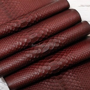 May include: A deep burgundy material featuring a distinct, raised scale pattern across its surface. The texture mimics the appearance of snake skin with overlapping, uniform scales. The text AcalapatiBali is visible across the center.