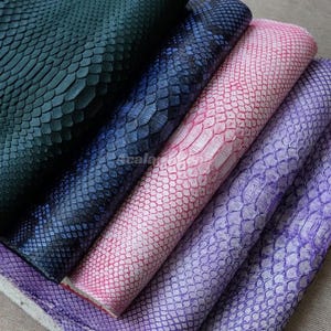 May include: Five stacked sheets of textured material featuring a repeating scale pattern. The colors include dark green, deep blue, light pink with white highlights, and two shades of purple, all displaying a consistent embossed reptile skin design.