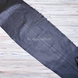 May include: A dark navy blue snakeskin leather hide featuring a distinct, repeating scale pattern across the entire surface. The material displays a textured, organic appearance with a central row of larger, elongated scales flanked by smaller scales.