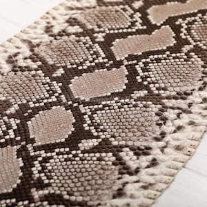 May include: A textured material featuring a repeating snakeskin pattern in shades of dark brown, light brown, and cream. The surface displays a detailed, scaled appearance with a geometric arrangement of dark brown lines forming a diamond-like grid.