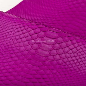 May include: A vibrant magenta material featuring a distinct, raised scale pattern across the surface. The texture mimics a reptile skin with overlapping, diamond-shaped segments. The text AcalapatiBali is printed in a light color across the center.