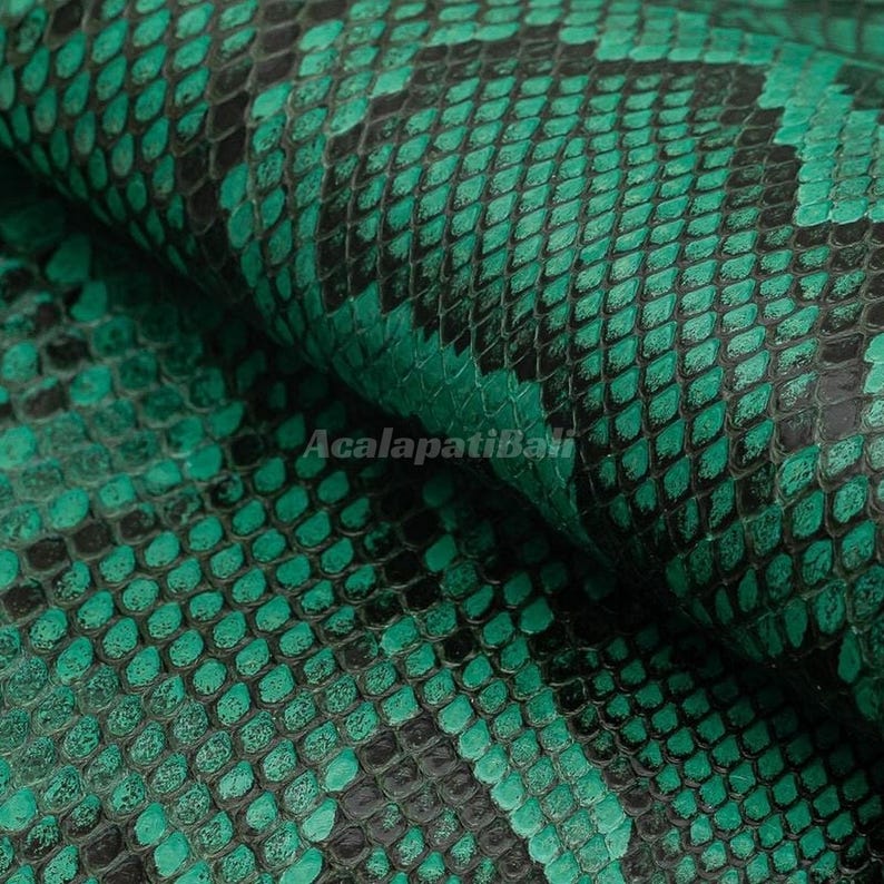May include: A textured material featuring a repeating scale pattern in vibrant emerald green and deep black. The surface displays a distinct, overlapping organic scale structure with a glossy finish and the text AcalapatiBali visible.