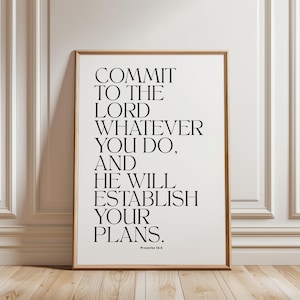 May include: A rectangular wall art print in a light wood frame featuring black serif typography on a white background. The text reads: COMMIT TO THE LORD WHATEVER YOU DO, AND HE WILL ESTABLISH YOUR PLANS. Proverbs 16:3 is printed at the bottom.