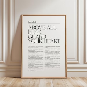 Op de afbeelding: Een ingelijste wandkunstprint met de tekst Proverbs 4, Above All Else, Guard Your Heart, gevolgd door de volledige bijbelse hoofdstuktekst in een strak, zwart schreeflettertype op een witte achtergrond, in een eenvoudige lichthouten lijst.