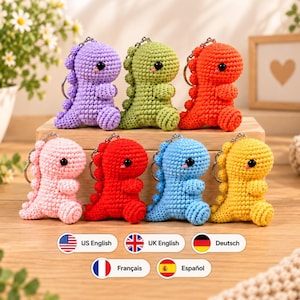 May include: Seven crochet dinosaur keychains in various colors including purple, light green, orange, light pink, red, blue, and yellow. Each small stuffed creature features a rounded head, black bead eyes, a tiny pink tongue, and a metal keyring.