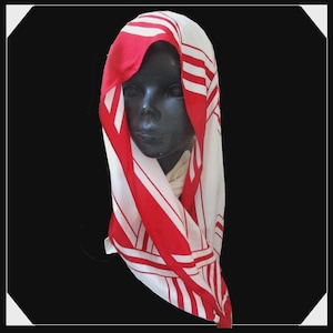 May include: A square scarf featuring a bold geometric pattern of vibrant red and crisp white stripes. The fabric is draped over a dark mannequin head, showcasing the contrasting linear design that runs across the entire surface of the accessory.