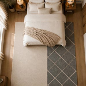 May include: A large rectangular area rug featuring a split design with a solid cream-colored section and a dark gray section patterned with a white diamond grid. The rug is positioned under a bed with cream bedding and a tan throw blanket.