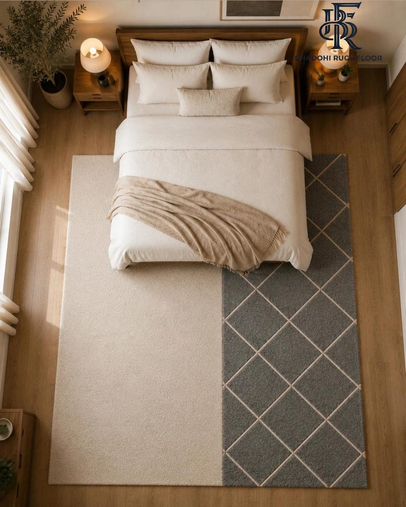 May include: A large rectangular area rug featuring a split design with a solid cream-colored section and a dark gray section patterned with a white diamond grid. The rug is positioned under a bed with cream bedding and a tan throw blanket.