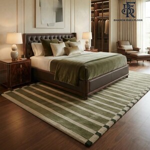 May include: A rectangular area rug featuring a striped pattern in alternating shades of olive green and cream. The rug is positioned on a dark wood floor beneath a bed with a dark brown headboard, two bedside lamps, and matching bedding.