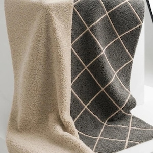 May include: A plush, textured rug featuring a two-tone design with a solid beige section and a dark gray section adorned with a white diamond grid pattern. The logo for Bhadohi Rugs Floor is visible in the upper right corner of the image.
