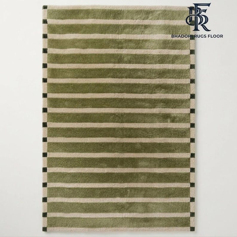May include: A rectangular area rug featuring horizontal stripes in olive green and beige. The rug has a border with a repeating pattern of small dark green squares. The text BHADOHI RUGS FLOOR is visible in the top right corner of the image.