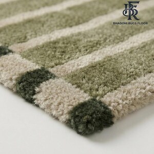 May include: A plush, high-pile area rug featuring alternating horizontal stripes in shades of sage green, olive green, and cream. The rug has a thick, textured surface and includes the logo text BHADOHI RUGS FLOOR in the upper right corner.