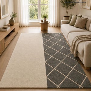 May include: A rectangular area rug featuring a split design with one half in solid cream and the other half in dark gray with a white diamond grid pattern. The rug is positioned on a light wood floor in a room with a sofa and wooden furniture.
