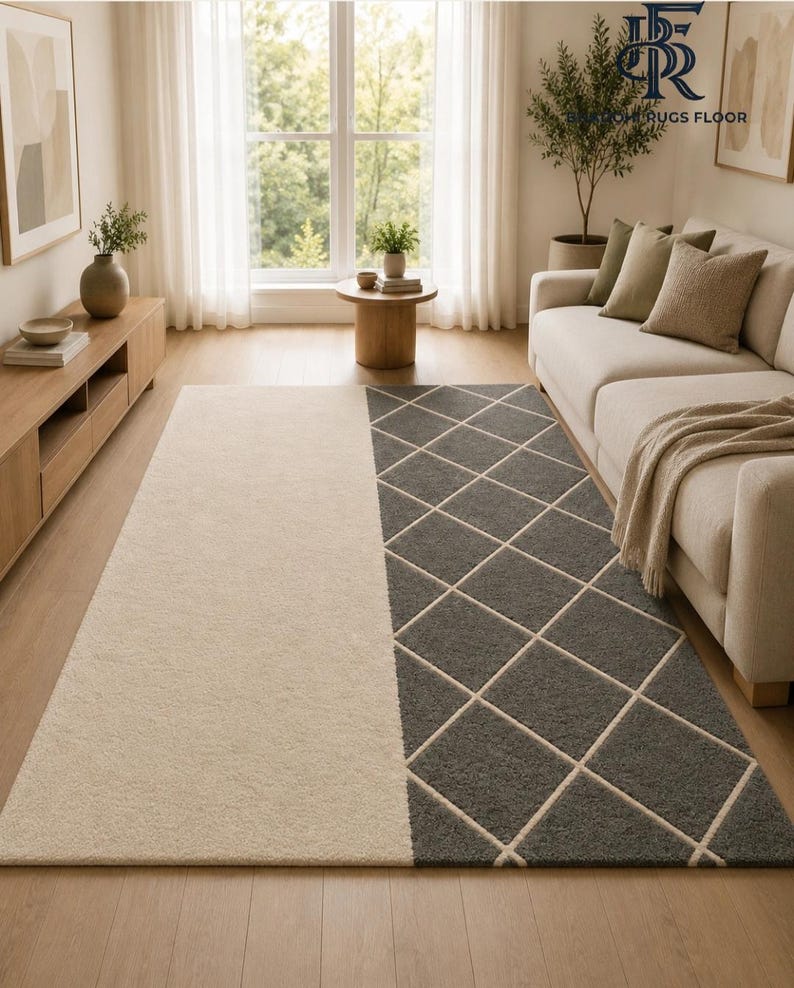 May include: A rectangular area rug featuring a split design with one half in solid cream and the other half in dark gray with a white diamond grid pattern. The rug is positioned on a light wood floor in a room with a sofa and wooden furniture.