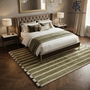 May include: A rectangular area rug featuring a pattern of alternating olive green and cream-coloured horizontal stripes. The rug is positioned beneath a tufted upholstered bed frame with white bedding, two nightstands with lamps, and a chandelier.