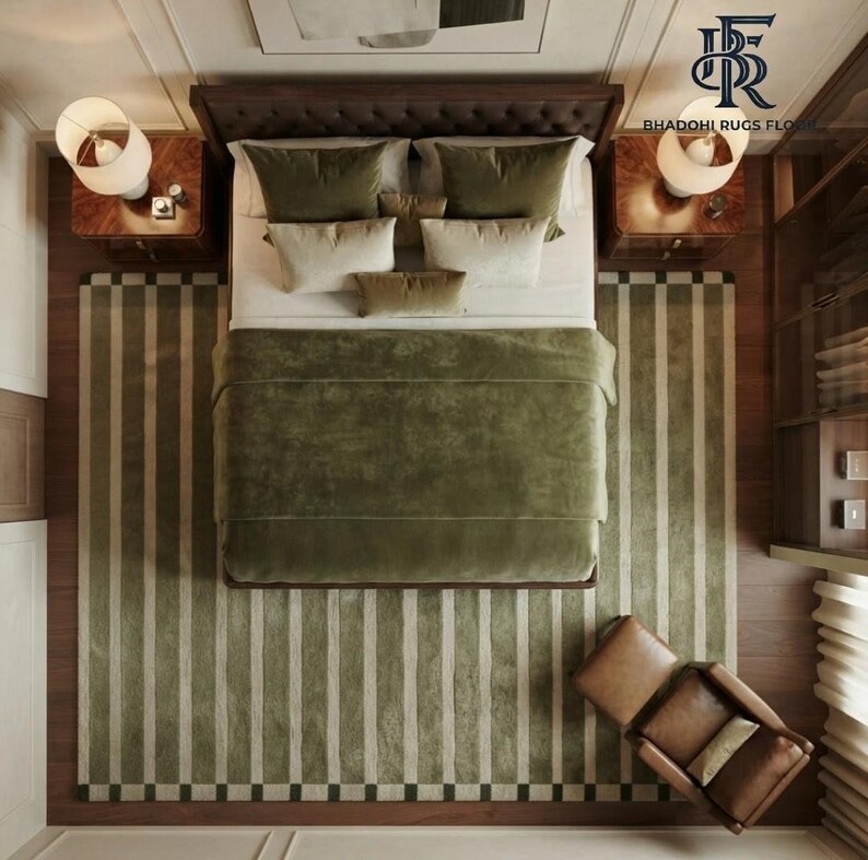 May include: A top-down view of a bedroom featuring a dark wood bed frame with a tufted headboard, covered in a solid olive green duvet and various pillows. Two wooden nightstands with white lamps flank the bed, set upon a striped olive and cream rug.