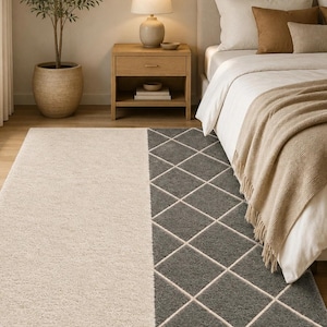 May include: A rectangular area rug featuring a split design with one half in solid cream and the other half in dark gray with a white diamond grid pattern. The rug has a textured, shaggy pile surface and is positioned on a wooden floor.