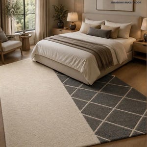 May include: A rectangular area rug featuring a split design with a solid cream-colored section on the left and a dark gray section on the right, which is decorated with a white diamond grid pattern. The rug is positioned on a wooden floor.