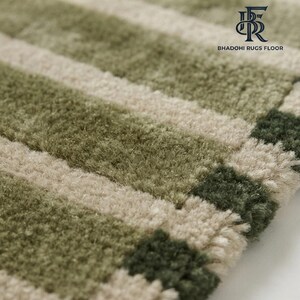 May include: A tufted rug featuring a repeating pattern of horizontal stripes in shades of sage green, olive green, and cream. The surface has a thick, textured pile. The top right corner displays the logo and text BHADOHI RUGS FLOOR.