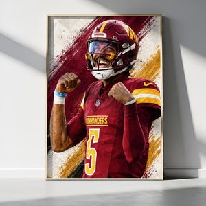 May include: A framed poster featuring a football player in a burgundy and gold Commanders jersey with the number 5, wearing a matching helmet and face mask, celebrating with fists raised. The background has a dynamic, brush-stroke artistic effect.