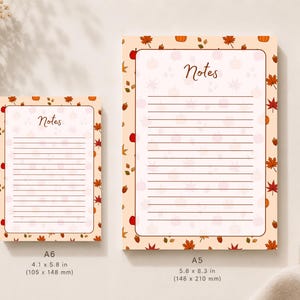 May include: Two rectangular note pads with a light peach background featuring a pattern of autumn leaves, acorns, and pumpkins. The pads have the word Notes printed at the top and horizontal lines. The A6 pad is 105 by 148 mm and the A5 is 148 by 210 mm.
