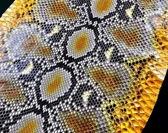 Puede incluir: Una pieza de piel de serpiente con un patrón repetitivo de escamas amarillas, blancas y negras. La textura se compone de pequeñas escamas superpuestas dispuestas en forma de diamante sobre la superficie del material.