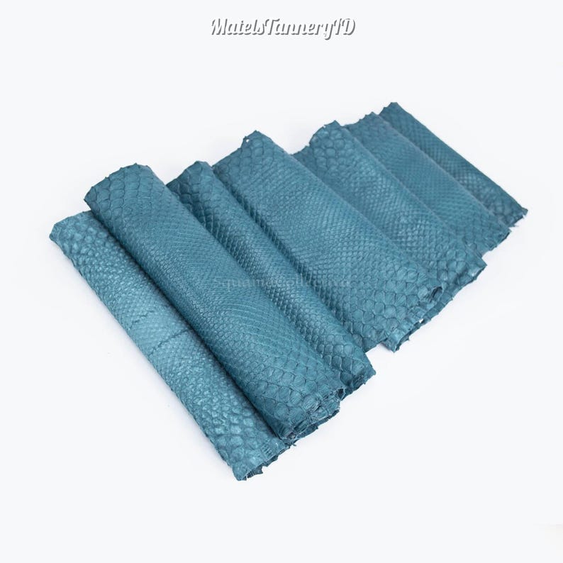 Puede incluir: Una colecci&oacute;n de piezas de piel de serpiente de color verde azulado dispuestas en un patr&oacute;n superpuesto. Cada pieza presenta un patr&oacute;n de escamas texturizado distintivo en la superficie. El texto MatelsTanneryID es visible arriba.