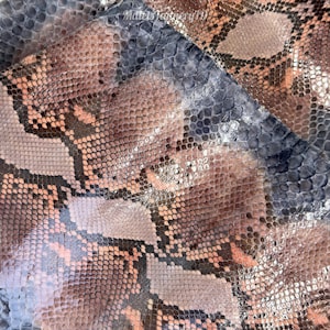 May include: A piece of textured snakeskin leather featuring a repeating scale pattern in shades of dusty pink, muted brown, and slate gray. The surface displays a natural organic arrangement of scales with the text MatelsTannery19 visible.