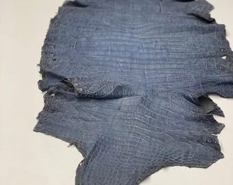 May include: A blue crocodile skin hide featuring a distinct textured scale pattern across the entire surface. The leather is laid flat and displays the natural shape of the animal hide with the text MatelsTanneryID visible at the top.