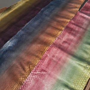 Peut inclure: Une longue pièce rectangulaire de cuir de serpent présentant un motif dégradé multicolore vibrant qui passe par des nuances de jaune, violet, bleu, marron, rose et vert. Le texte MatelsTanneryID est imprimé sur la partie supérieure.
