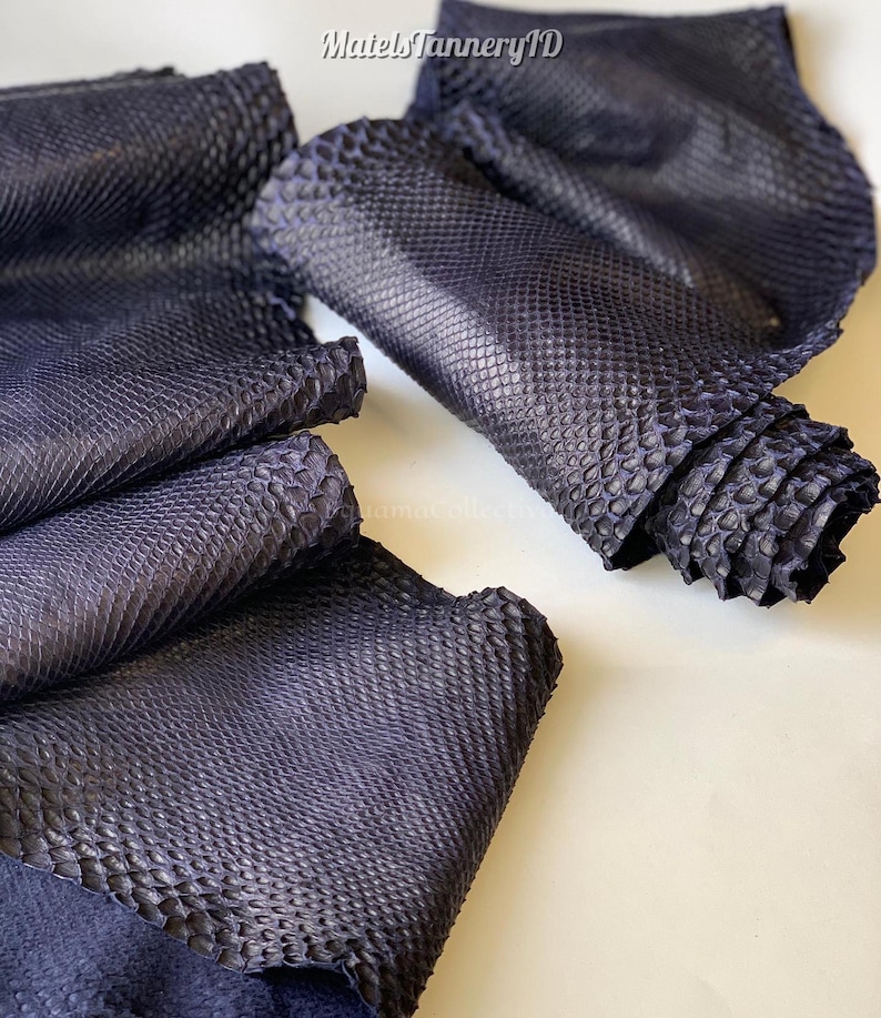 May include: Dark navy blue snakeskin leather sheets with a distinct, raised scale texture. The material is folded and layered, showing a matte finish. The text MatelsTanneryID is visible at the top center of the image against the dark leather.