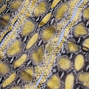 May include: A textured snake skin material featuring a repeating pattern of yellow, black, and white scales. The surface displays a distinct diamond-shaped scale arrangement with the text MatelsTanneryID visible at the top center of the material.