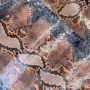 Op de afbeelding: Een stuk slangenleer met een herhalend ruitpatroon in tinten oudroze, gedempt bruin en leigrijs. Het oppervlak heeft een getextureerd, schubachtig uiterlijk met een subtiele glans. De tekst MatelsTannery19 is zichtbaar.
