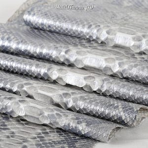 May include: A silver-toned snakeskin leather hide with a metallic finish and a distinct, raised scale pattern. The surface features a repeating, textured texture with the text MatelsTanneryID visible at the top of the hide.