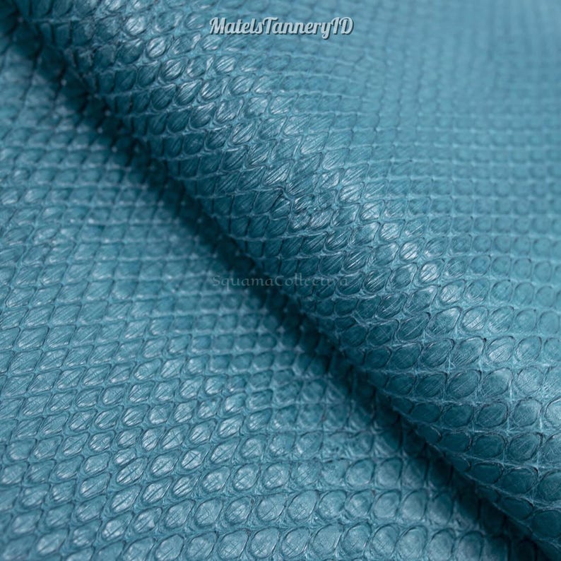 Puede incluir: Una l&aacute;mina de cuero color verde azulado con un patr&oacute;n distintivo de escamas en forma de diamante en relieve que se repite por toda la superficie. El material tiene un acabado mate e incluye el texto MatelsTanneryID y SquamaCollectiva impreso.