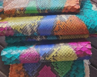 May include: A stack of multi-coloured snakeskin leather sheets featuring a repeating diamond scale pattern in vibrant shades of pink, blue, yellow, orange, and green. The text MatelsTanneryID is visible at the top of the top leather sheet.